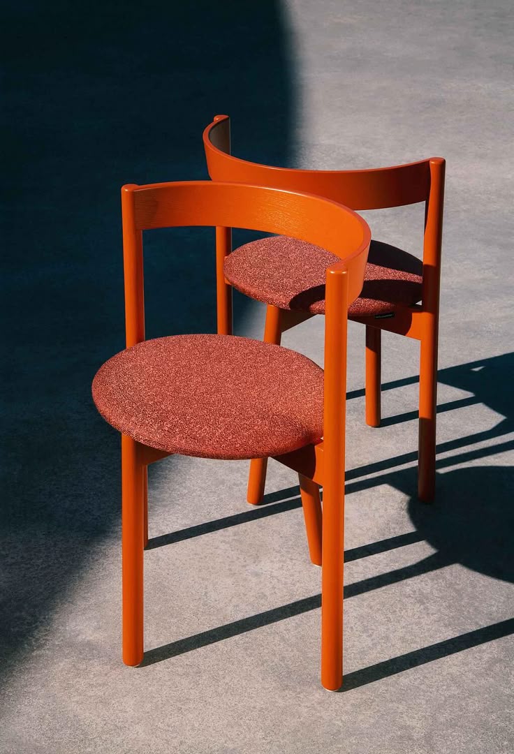 Two orange chairs casting long shadows across a concrete floor