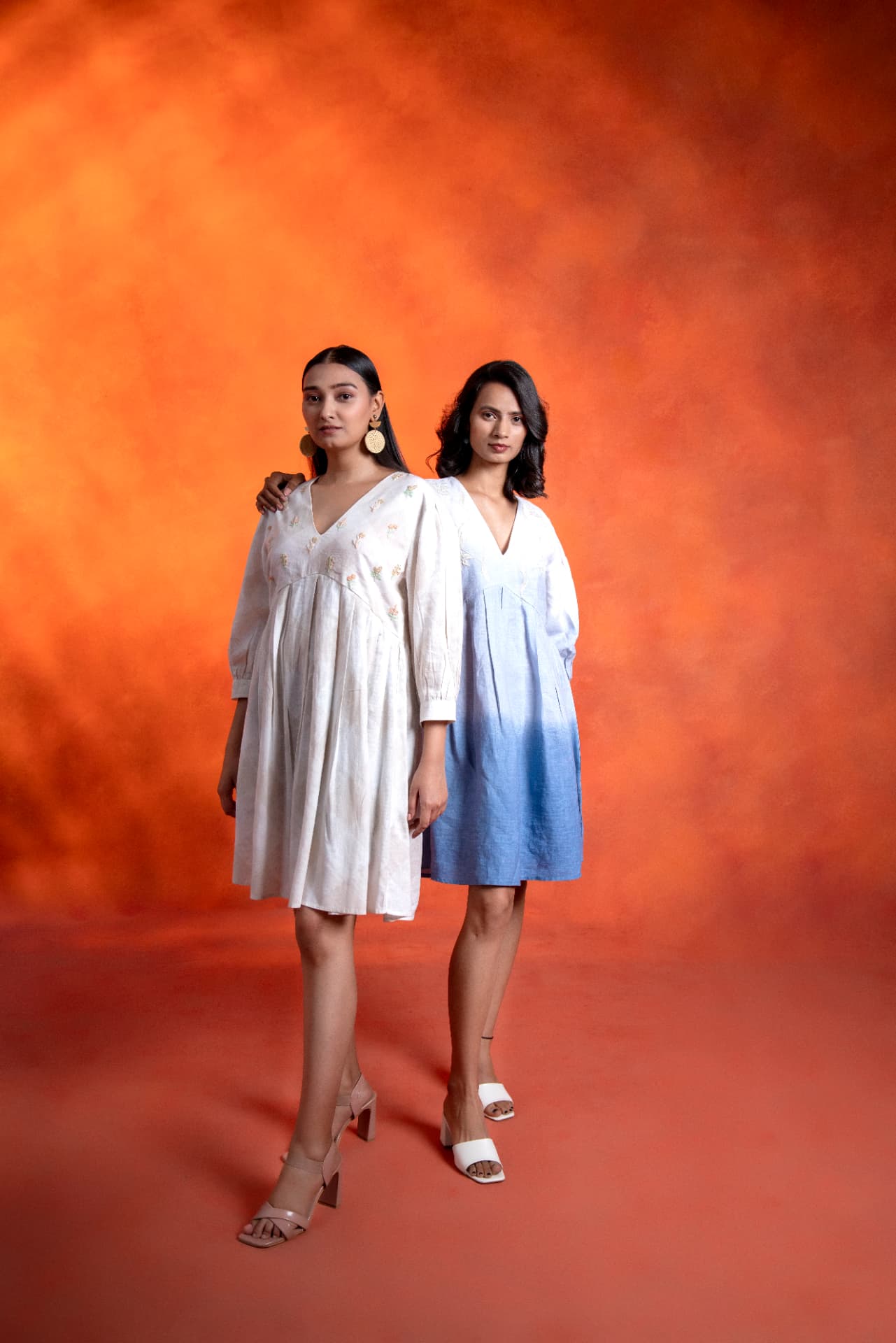 Two models in linen dresses on a warm orange backdrop